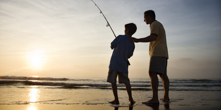 Father and son fishing in ocean surf at sunset.